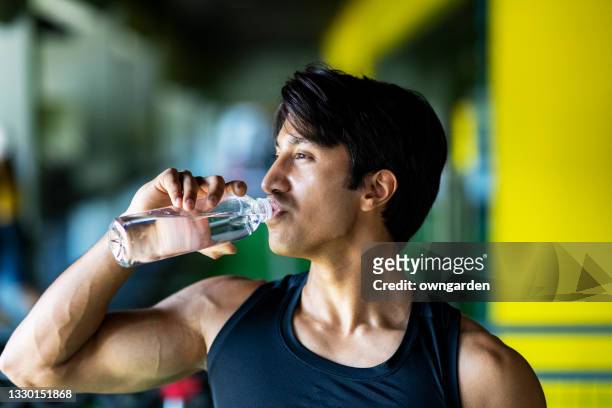 young athletic man drinking water in gym. - lap body area stock-fotos und bilder