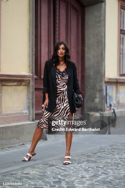 Ioana Visanescu wears a necklace, a black oversized blazer jacket, a black and beige zebra pattern printed midi slit dress with embroidery, a black...