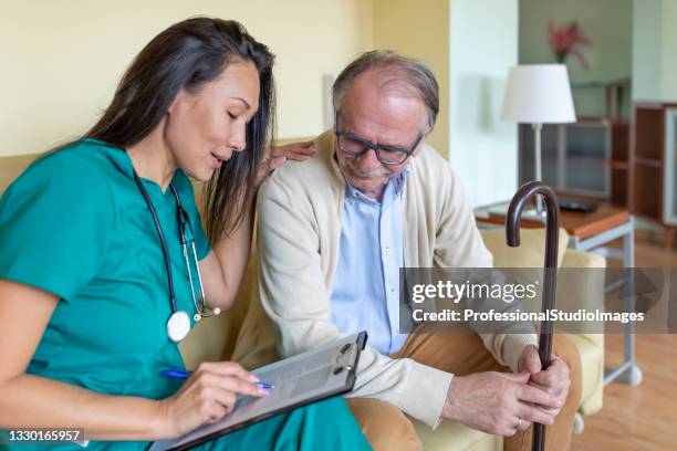sick old man is receiving advice from nurse in home visit. - elderly receiving paperwork stock pictures, royalty-free photos & images