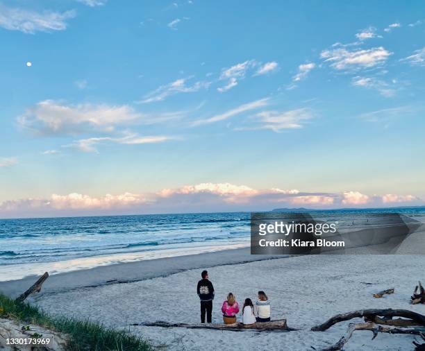 friends at beach look to waves and moon at dusk - australian winter stockfoto's en -beelden
