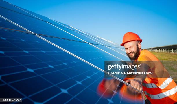 installing of stand-alone solar photo voltaic panel system. technician in hard-hat, mounting big shiny solar module  on green summer view background. alternative energy concept. - hard choice stock pictures, royalty-free photos & images