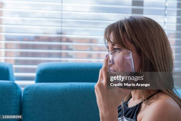 woman sitting on the sofa in her living room, drinking a red wine while lying on her sofa enjoying a quiet afternoon - alcoholisme stockfoto's en -beelden