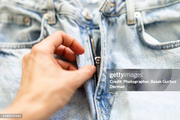 a woman hand holding / touching the zip of a pair of denim jean trousers - reißverschluß stock-fotos und bilder