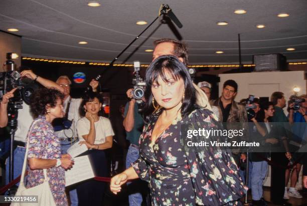 American comedian Roseanne Arnold, wearing gold hoop earrings and a black dress with colour butterfly motifs, with her husband, American actor and...