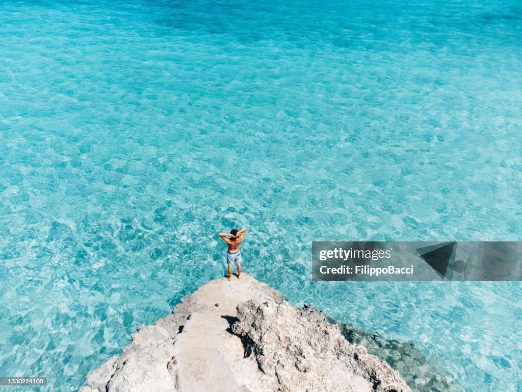 両手を広げて美しいターコイズブルーの海を眺めた若者の空中写真