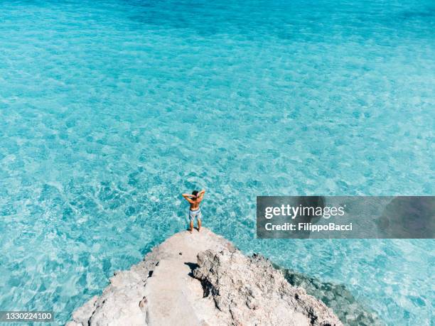 aerial view of a young man admiring a beautiful turquoise sea with open arms - inviting gesture stockfoto's en -beelden