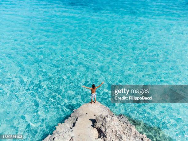 vista aérea de un joven admirando un hermoso mar turquesa con los brazos abiertos - islas baleares fotografías e imágenes de stock