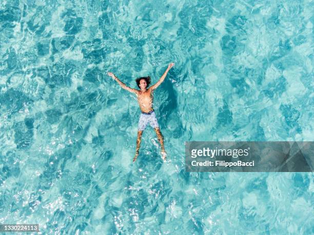 aerial view of a man relaxing himself in a beautiful transparent turquoise sea - luxury swimming pool stock pictures, royalty-free photos & images