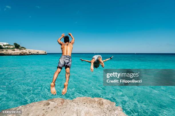 two friends are diving in the sea from a cliff - beach stock pictures, royalty-free photos & images