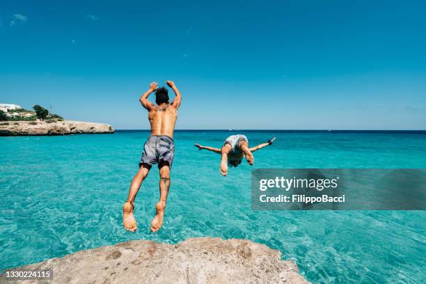 two friends are diving in the sea from a cliff - spanish imagens e fotografias de stock