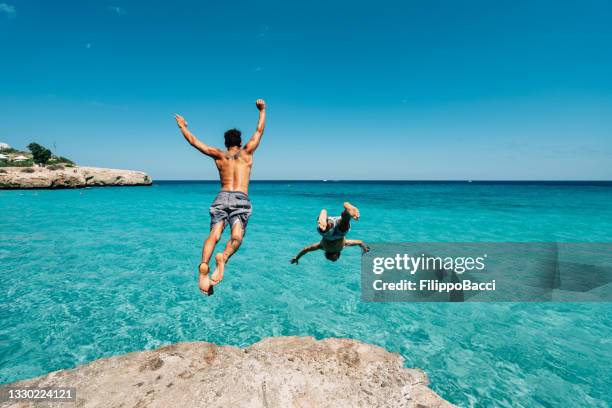 two friends are diving in the sea from a cliff - ensolarado imagens e fotografias de stock