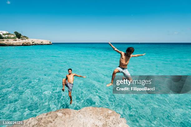 zwei freunde tauchen von einer klippe aus im meer - insel mallorca strand stock-fotos und bilder