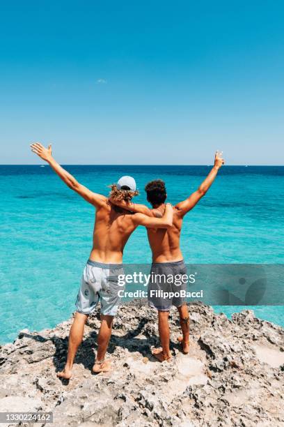 two friends are standing on a cliff looking at the sea - caribbean party stock pictures, royalty-free photos & images