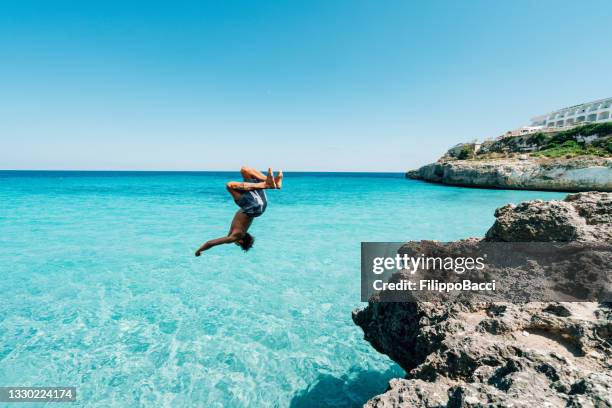 young man is diving in the sea from a cliff doing a backflip - achterwaartse salto stockfoto's en -beelden