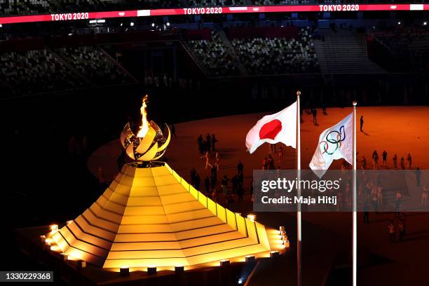 Detailed view of the Olympic cauldron lit next to the Japanese and Olympic flags during the Opening Ceremony of the Tokyo 2020 Olympic Games at...