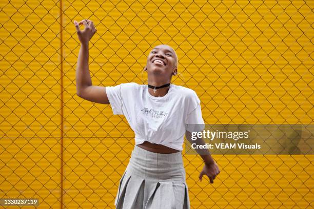 cheerful black african woman with short hairstyle posing laughing in front of a fence on a yellow wall. - female navel ストックフォトと画像