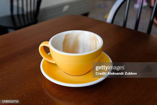 an empty dirty coffee cup of bright yellow color, on a brown wooden table in a cafe or restaurant. the coffee break has ended. - マグカップ ストックフォトと画像