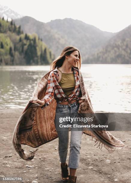 a lonely free happy woman in casual clothes travels runs hikes covered with a plaid enjoying solitude on vacation on the river bank in nature in autumn outdoors - woman in a shawl stock pictures, royalty-free photos & images