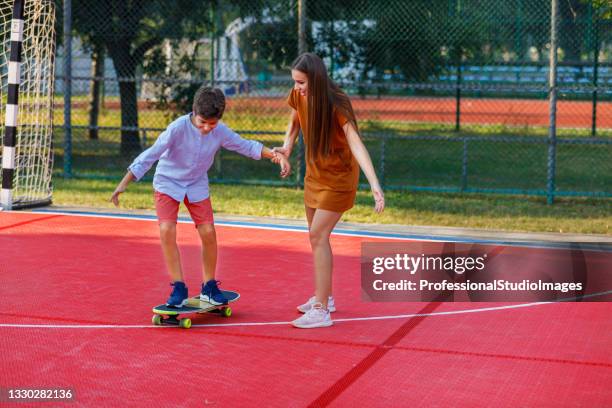 happy mother is helping her son to learn to ride a long board. - preteen model stock pictures, royalty-free photos & images