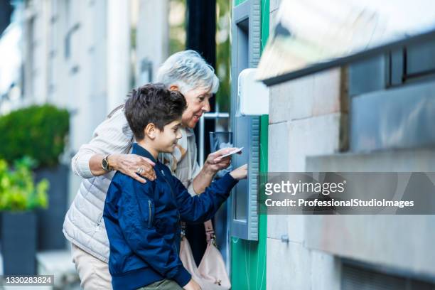 senior woman is using atm with her grandchild. - grandma invoice stock pictures, royalty-free photos & images