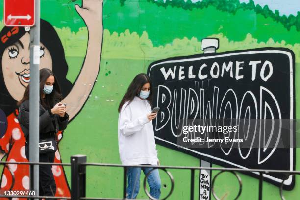 Two girls in masks walk past a "welcome to Burwood" mural on July 24, 2021 in Sydney, Australia. New South Wales Premier Gladys Berejiklian declared...