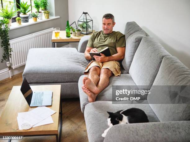 shot of a mature man writing in a notebook while working on the sofa at home - 2020 vision stock pictures, royalty-free photos & images