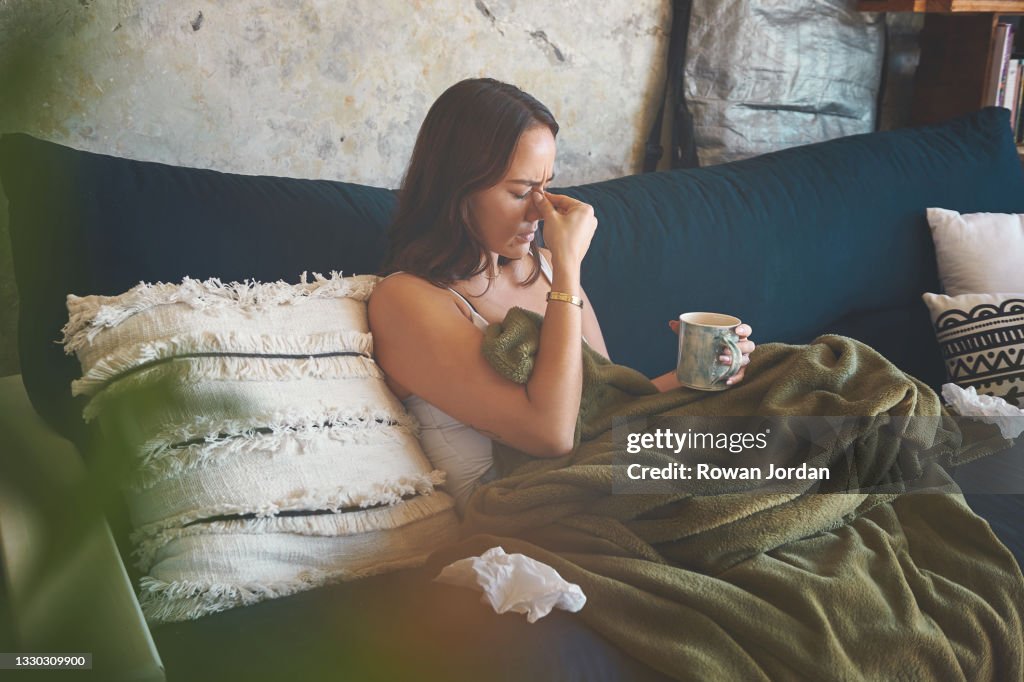 Shot of a young woman suffering from a headache and feeling sick on the sofa at home