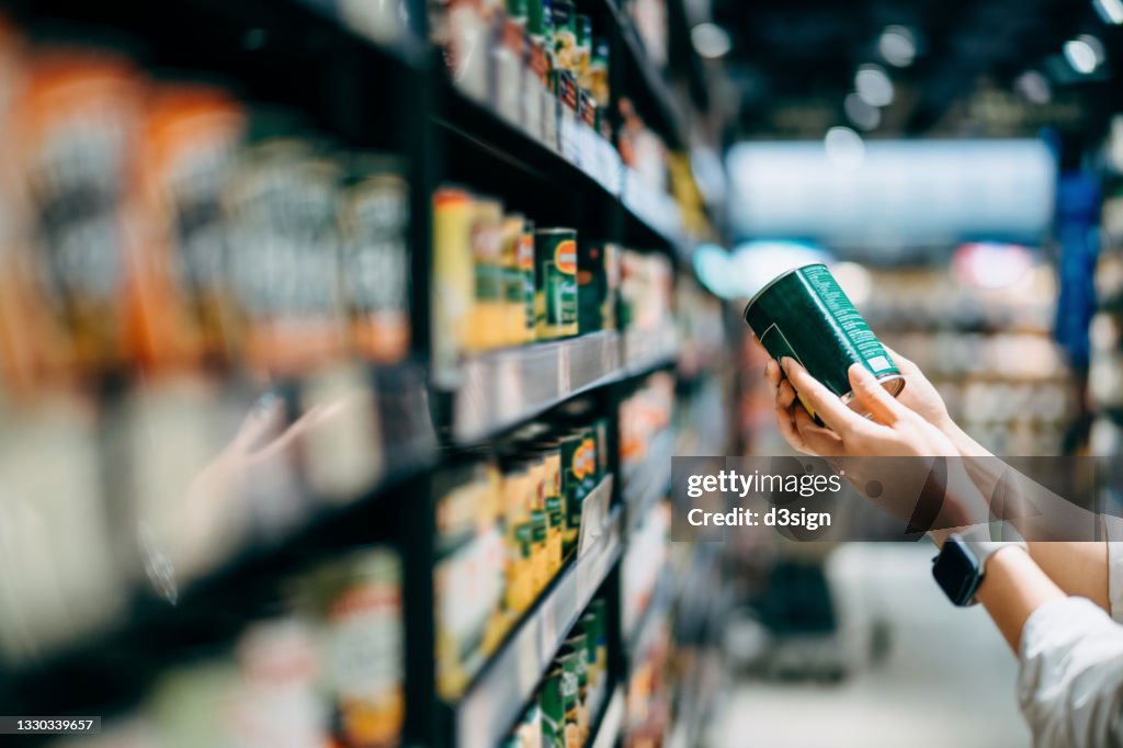 Close up of a woman grocery shopping in supermarket. Holding a tin can and reading the nutrition label at the back