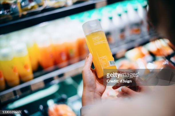 over the shoulder view of young asian woman grocery shopping in supermarket. she is reading the nutrition label on the bottle of fresh orange juice - orange juice stock-fotos und bilder