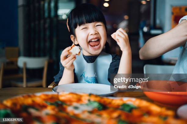 happy little asian girl enjoying pizza lunch in an outdoor restaurant, with a giant pizza in front of her on the dining table. looking at camera and smiling joyfully. eating out lifestyle - familie eten stockfoto's en -beelden