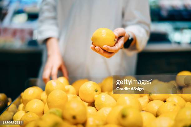 cropped shot of young asian woman grocery shopping for fresh organic fruits and vegetables in supermarket, close up of her hands choosing fresh lemons. healthy eating lifestyle - produce aisle photos et images de collection