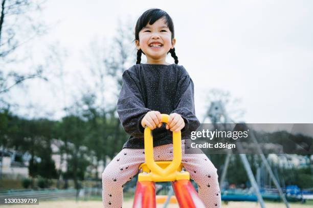 lovely little asian girl smiling joyfully, having fun playing on a seesaw in the outdoor playground - china games day 1 fotografías e imágenes de stock