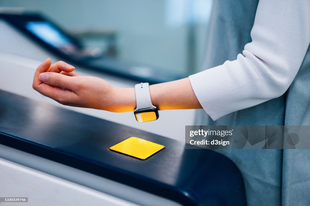 Close up of young Asian woman checking in at subway station, making a quick and easy contactless payment for subway ticket via smartwatch. NFC technology, tap and go concept