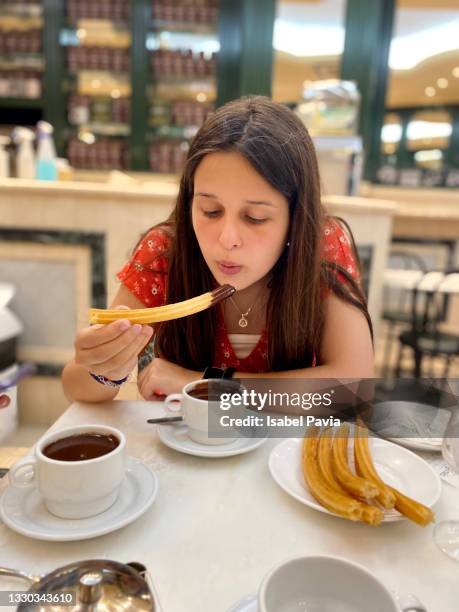 young hispanic woman eating chocolate with churros - churro stockfoto's en -beelden