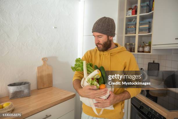 el hombre guarda los comestibles vegetales en la cocina - dieta a base de plantas fotografías e imágenes de stock