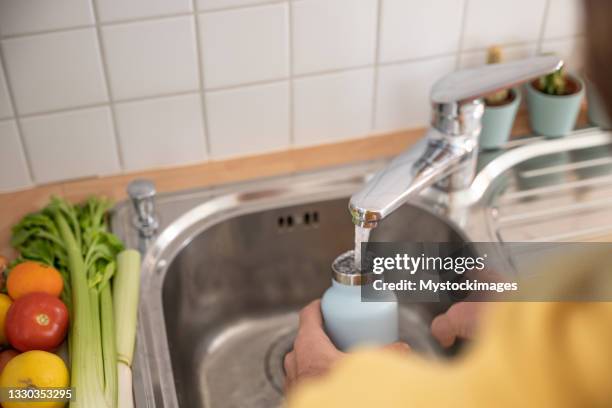 homem enche garrafa de água reutilizável na cozinha - reusable water bottle - fotografias e filmes do acervo