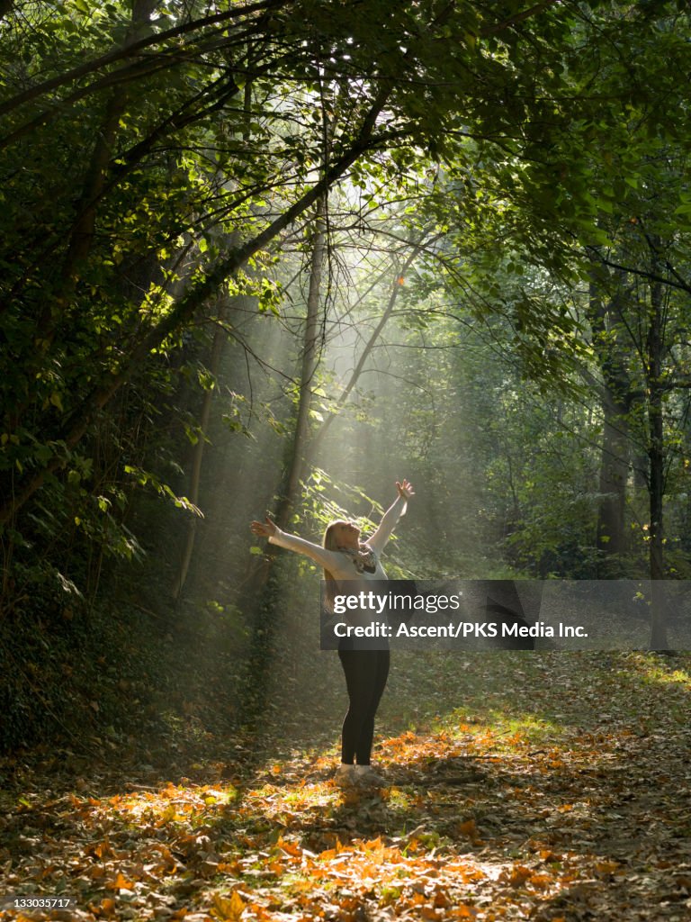 Woman stretches arms upwards into shaft of light