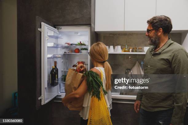 woman putting groceries away in the fridge - opbergen stockfoto's en -beelden