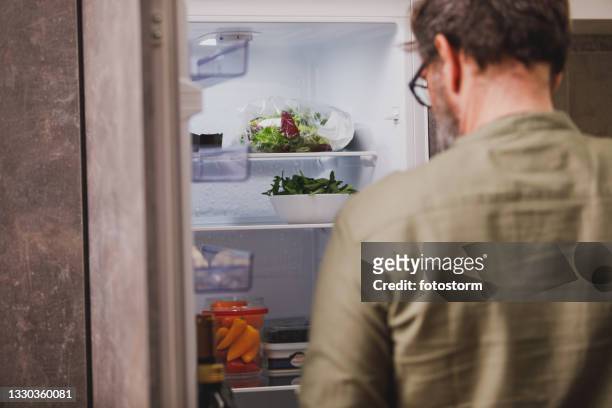 rückansicht des mannes, der vor einem offenen kühlschrank steht - open fridge stock-fotos und bilder