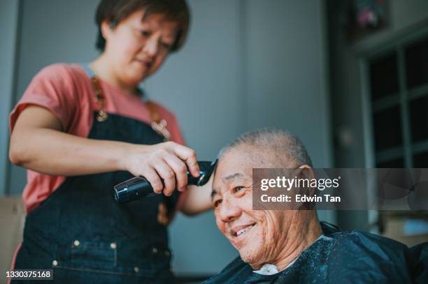 asiatische chinesische frau, die tagsüber haare für ihren vater im rollstuhl in der garage des vorgartens schneidet - half shaved hairstyle stock-fotos und bilder