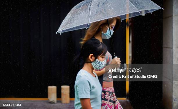 mother and daughter under an umbrella on a rainy day - mother protecting from rain stockfoto's en -beelden