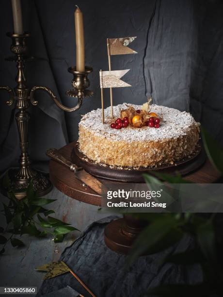 food photography of cake napoleon on wooden stand side view with festive decor (paper flags, red berries and physalis) in holiday interior with candles in a candelabrum on gray background close up - cake flag stock pictures, royalty-free photos & images