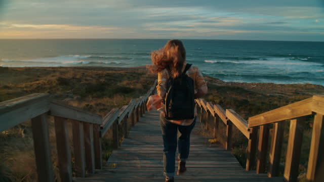 Young female traveler run to ocean at sunset beach