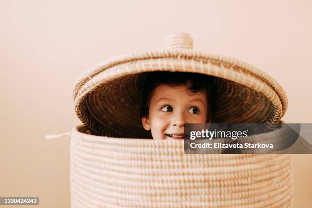 portrait of a cheerful happy emotional face of a child, a teenage boy looking out of a children's wicker basket, playing hide-and-seek in the children's room at home - kid hide and seek stock pictures, royalty-free photos & images