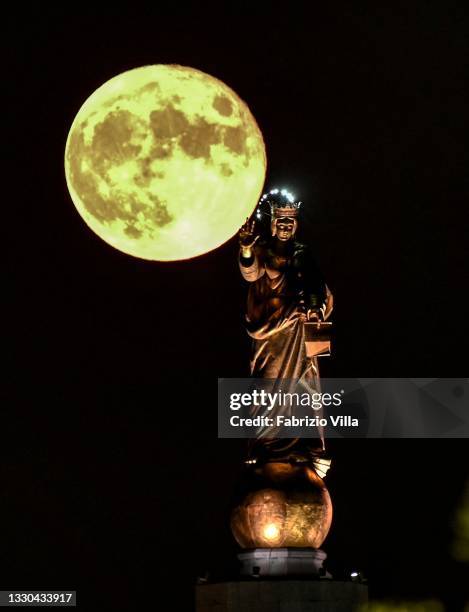 Full moon with the Madonnina of the Strait of Messina. Sicily on July 24, 2021 in Messina, Italy. The statue of “Madonna della Lettera” is erected at...