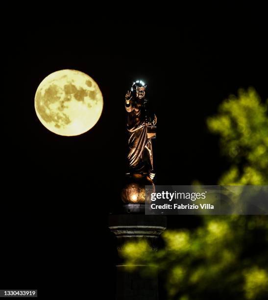 Full moon with the Madonnina of the Strait of Messina. Sicily on July 24, 2021 in Messina, Italy. The statue of “Madonna della Lettera” is erected at...