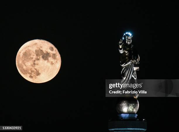 Full moon with the Madonnina of the Strait of Messina. Sicily on July 24, 2021 in Messina, Italy. The statue of “Madonna della Lettera” is erected at...