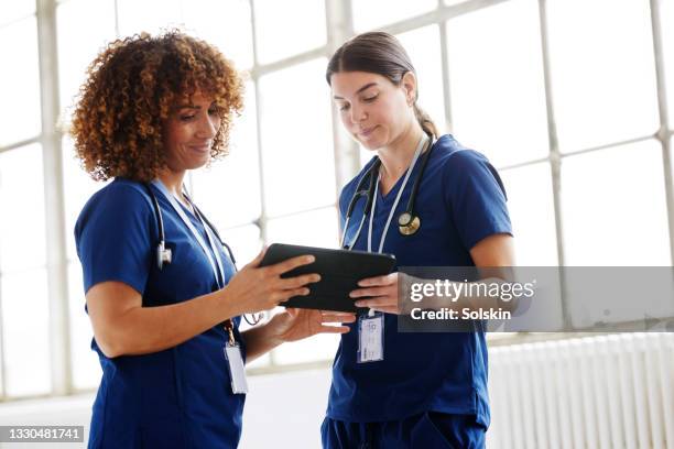 two healthcare professionals in conversation, looking at digital tablet - medizinerkleidung stock-fotos und bilder