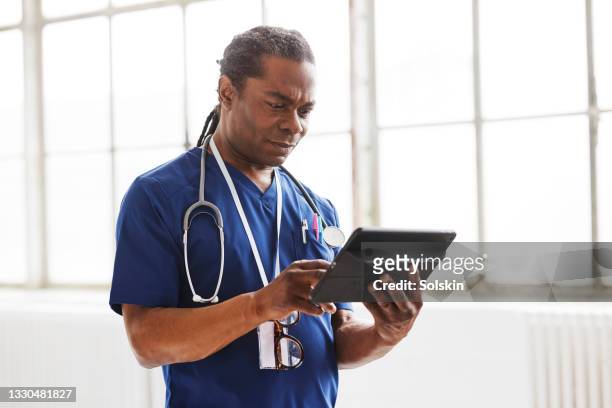 doctor in scrubs reading digital medical documents - graphics tablet stock pictures, royalty-free photos & images