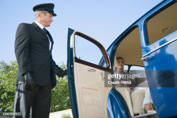 chauffeur opening door of a vintage car for female passenger - símbolo de status imagens e fotografias de stock